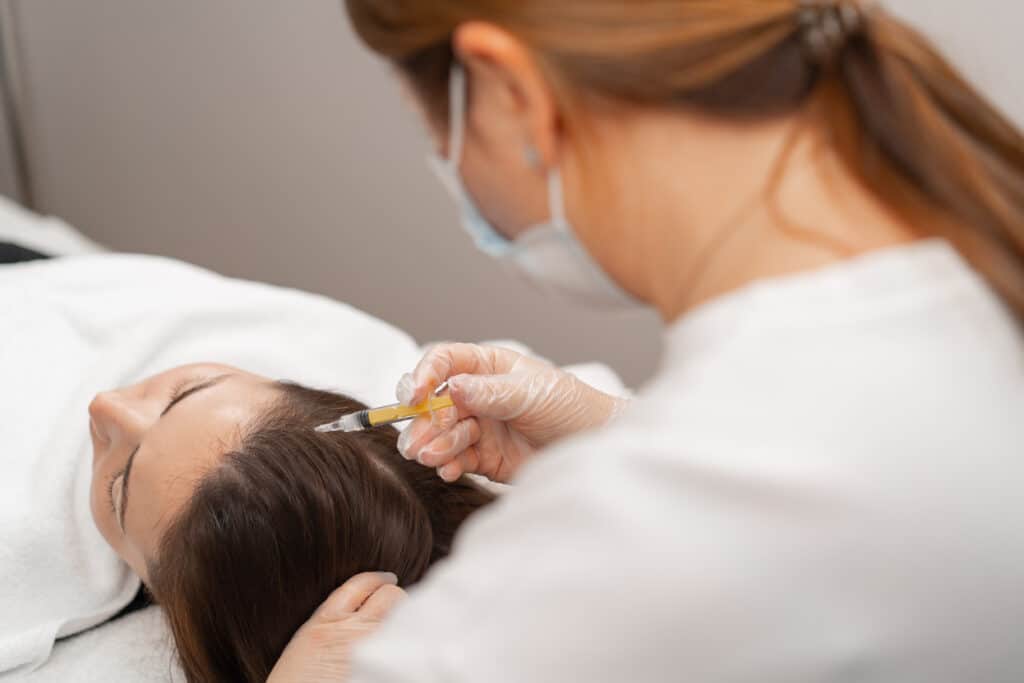 A beautician makes injections into the scalp for hair growth Mesotherapy for hair growth and strengthening in beauty salon A procedure against hair loss